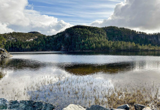 Udsigt over en rolig sø med træklædte bakker og dramatisk himmel, set fra en yurt i Lysøysundet, Sverige.