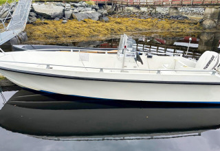 White motorboat docked at a small pier with rocky and seaweed-covered shore in Lysøysundet, Sweden.