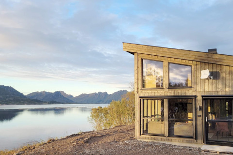Modernes Ferienhaus mit großen Fenstern und herrlichem Seeblick auf die Berge in Stokmarknes, Schweden.