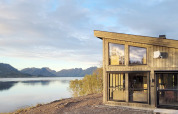Chalet moderne avec de grandes fenêtres, sur un lac avec vue sur les montagnes à Stokmarknes, Suède.