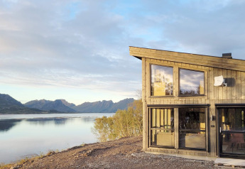 Modernes Ferienhaus mit großen Fenstern und herrlichem Seeblick auf die Berge in Stokmarknes, Schweden.