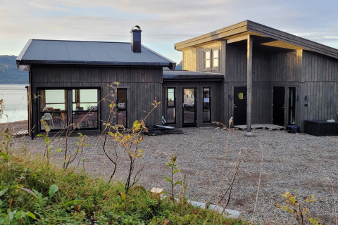 Maison de vacances moderne en bois sombre à Stokmarknes, Suède, avec grandes baies vitrées.