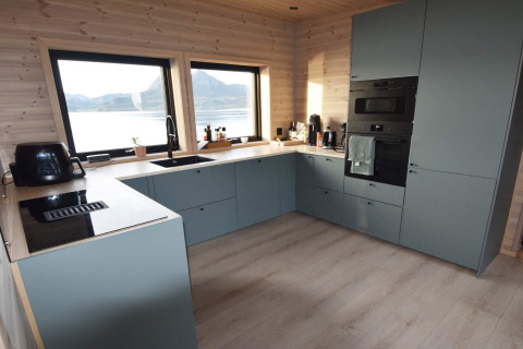 Moderne keuken met blauwe kasten, grote ramen en uitzicht op meer in de lodge van Stokmarknes, Zweden.