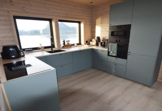 Cocina moderna con armarios azules, grandes ventanas y vistas al lago y montañas en Stokmarknes lodge.