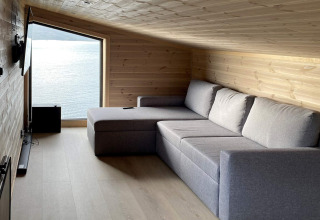 Stue i lodge '5 star holiday home in stokmarknes', Sverige, med grå sofa, trævægge og udsigt til sø.