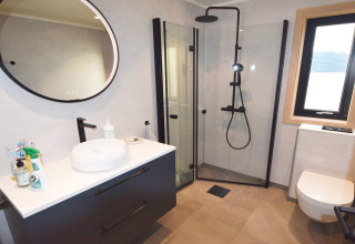Moderne badkamer met ronde spiegel, douchecabine, wastafel en raam in 5-sterren vakantiehuis Stokmarknes.