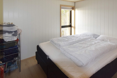 Lichte slaapkamer met tweepersoonsbed, wit beddengoed en draadrekken in vakantiehuis Stokmarknes.