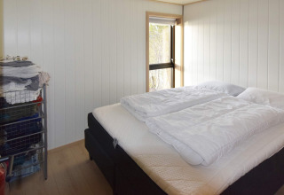 Helles Schlafzimmer mit Doppelbett, weißen Bettdecken und Drahtregalen in Ferienhaus in Stokmarknes.