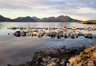 Både ligger forankret ved en stille havn ved 5-stjernet feriehus i Stokmarknes, med bjerge i baggrunden.
