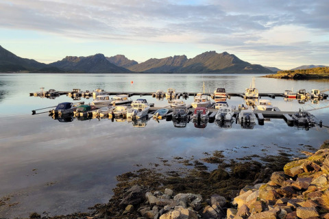 Barche ormeggiate su acque tranquille vicino alla casa vacanze 5 stelle a Stokmarknes, vista montagne.