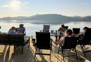 Gruppe mennesker slapper af på terrasse ved sø, bjerge i baggrunden, taget ved Stokmarknes lodge i Sverige.