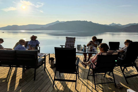 Groupe détendu sur terrasse au bord d’un lac, montagnes derrière, à 5 star holiday home in Stokmarknes, Suède.