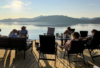 Groupe détendu sur terrasse au bord d’un lac, montagnes derrière, à 5 star holiday home in Stokmarknes, Suède.