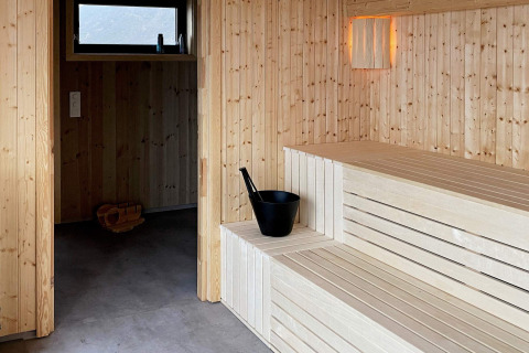 Binnenzicht van een moderne sauna met houten banken en emmer in een 5-sterren vakantiehuis in Stokmarknes, Zweden.