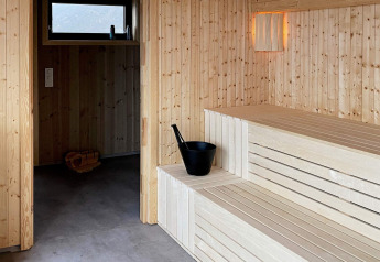 Innenansicht einer modernen Sauna mit Holzbänken und Eimer im 5-Sterne-Ferienhaus in Stokmarknes, Schweden.