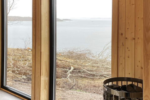 Vista desde una cabaña revestida de madera con grandes ventanas y estufa de sauna, con lago en Stokmarknes.