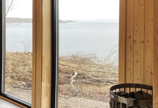 Vista da lodge con pannelli in legno, grandi finestre e stufa sauna, con panorama d’acqua a Stokmarknes.