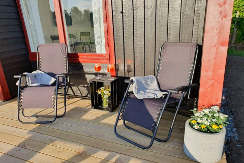 Due sedie reclinabili e un tavolino con bevande e fiori sul terrazzo di una cabina nera e rossa.