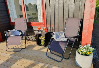 Deux chaises longues et une petite table avec boissons et fleurs sur la terrasse d’un chalet noir et rouge.