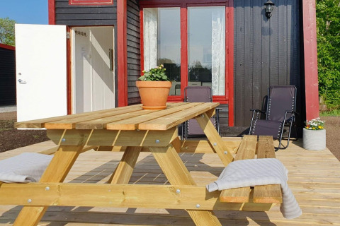 Terraza de madera con mesa de picnic y sillas reclinables frente a una cabaña negra y roja en KARLSKRONA, Suecia.