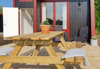 Terrasse en bois avec table de pique-nique et chaises longues devant un chalet noir et rouge à KARLSKRONA, Suède.