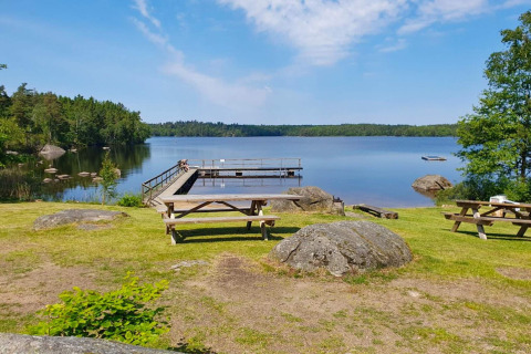 Picnicborde og badebro ved en sø omgivet af træer, set fra 4-stjernet feriehus i Karlskrona.