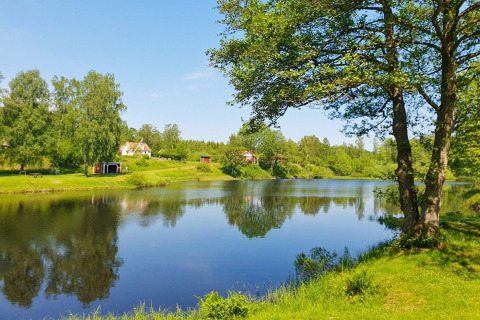 Vista panorámica de una cabaña junto al lago rodeada de árboles verdes en Karlskrona, Suecia, día soleado.
