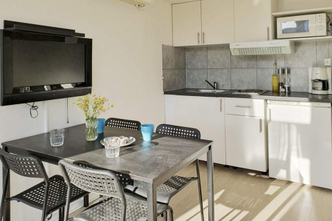 Cuisine et coin repas modernes avec table noire, quatre chaises et TV murale dans un chalet à Karlskrona.