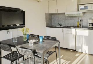 Cocina y comedor modernos con mesa negra, cuatro sillas y televisor en una cabaña en Karlskrona.