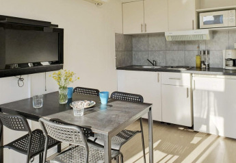 Moderne keuken en eethoek met zwarte tafel, vier stoelen en wand-tv in een chalet in Karlskrona.