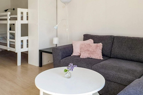 Gemütlicher Wohnraum mit grauem Sofa, rosa Kissen, weißem Tisch und Etagenbett in Karlskrona, Schweden.