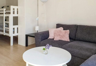 Salon avec canapé gris, coussins roses, table blanche et lits superposés dans un chalet à Karlskrona, Suède.