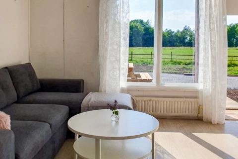 Lyst opholdsområde i 4-stjernet feriehus i Karlskrona, Sverige, med sofa, sofabord og udsigt til mark.
