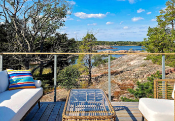 Moderne terrasse ved feriehus i VÄDDÖ, Sverige, med udsigt over skov og klippeøer mod vandet.