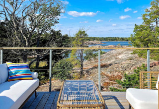 Zonnig terras bij vakantiehuis in VÄDDÖ, Zweden, met zicht op rotsen, water en groene natuur.