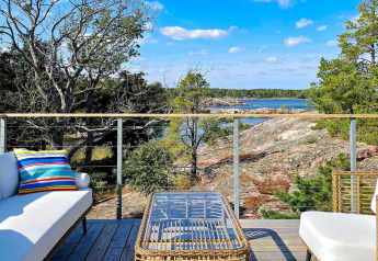 Terrasse moderne d'une maison de vacances à VÄDDÖ, Suède, surplombant la nature, les rochers et l'eau.