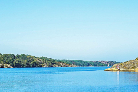 Rustig uitzicht op het water en de rotsachtige oever bij Nösund, Zweden, met zeilboot en groen.