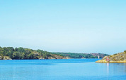 Smuk udsigt over vandet og klipper ved Nösund, Sverige, med en sejlbåd i det fjerne og grønne træer.