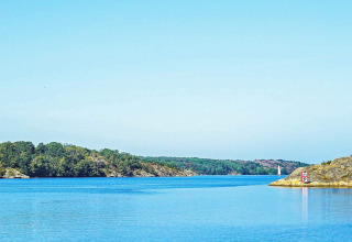 Rustig zicht op het water en de rotsachtige oever in Nösund, Zweden, met zeilboot en groene natuur.