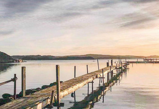 Molo in legno al tramonto presso il ‘4 person holiday home in Nösund’ in Svezia, acqua calma e colline lontane.