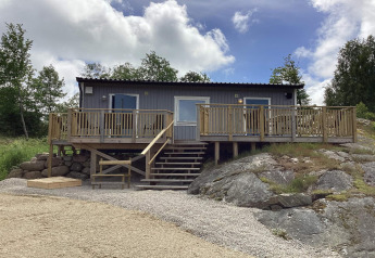 Vakantiehuis voor 4 personen in Nösund met houten terras, trap en rotsachtige omgeving onder een bewolkte lucht.