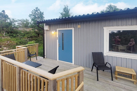 Terrasse en bois d'une maison de vacances à Nösund, Suède, avec chaises, table et cadre verdoyant.