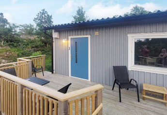 Træterrasse og blå dør ved sommerhus i Nösund, Sverige, med to stole, bord og naturskøn udsigt.