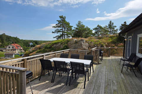 Amplia terraza de madera con mesa y sillas de comedor junto a una cabaña en Nösund, Suecia, paisaje.