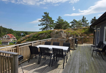 Ruim houten terras met eettafel en stoelen bij een huisje in Nösund, Zweden, uitzicht op heuvels.