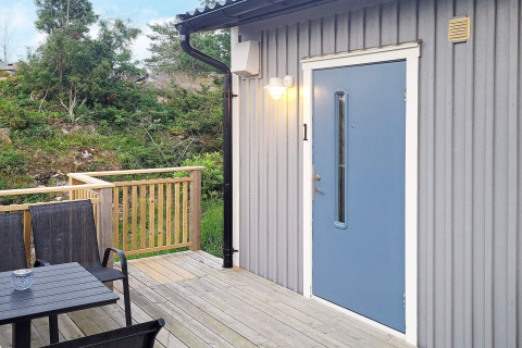 Buitenterras met zwarte stoelen en blauwe deur bij een blokhut in Nösund, Zweden.