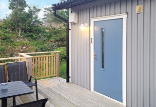 Buitenterras met zwarte stoelen en blauwe deur bij een blokhut in Nösund, Zweden.