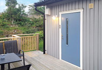 Buitenterras met zwarte stoelen en blauwe deur bij een blokhut in Nösund, Zweden.