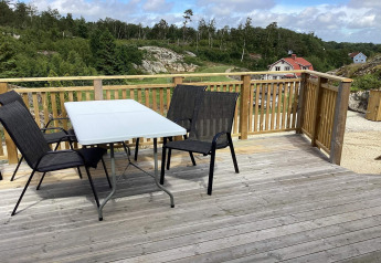 Udendørs terrasse med bord og stole på en hytte i Nösund, Sverige, omgivet af natur og huse.