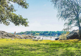 Zonnige dag aan het meer met rotsen, groene bomen en gras bij een vakantiehuisje in Nösund, Zweden.